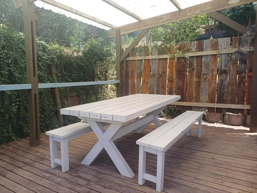 Covered wooden deck with white picnic table and benches overlooking garden