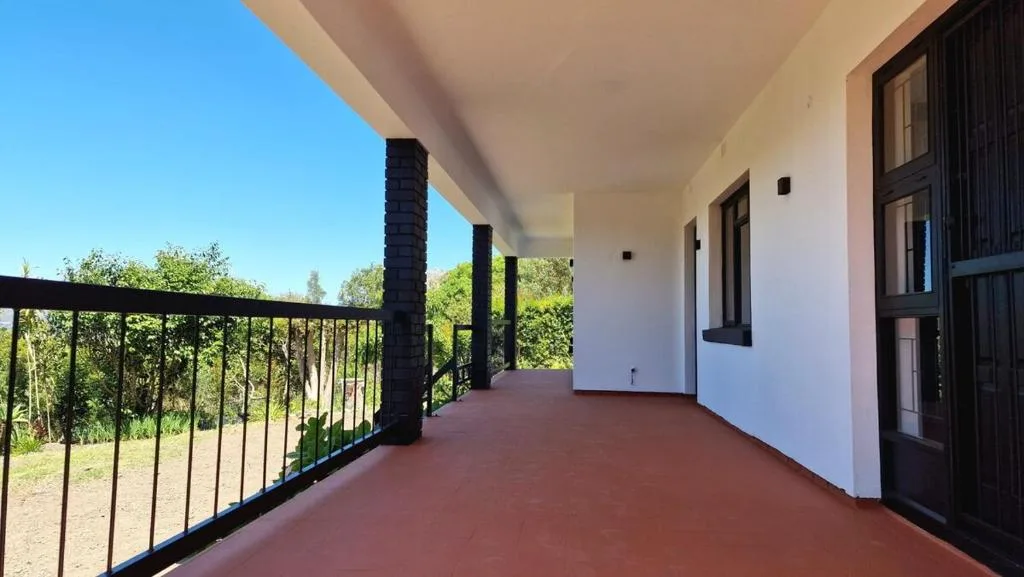 Spacious covered patio with red floor and black railing overlooking garden