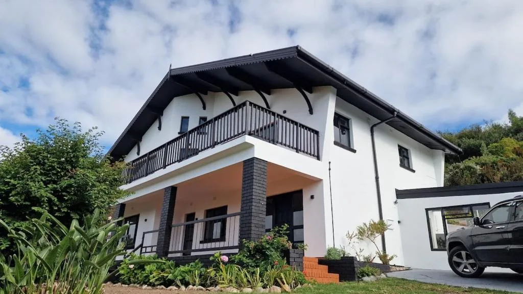 Modern white villa with black roof and upper balcony, garden surroundings
