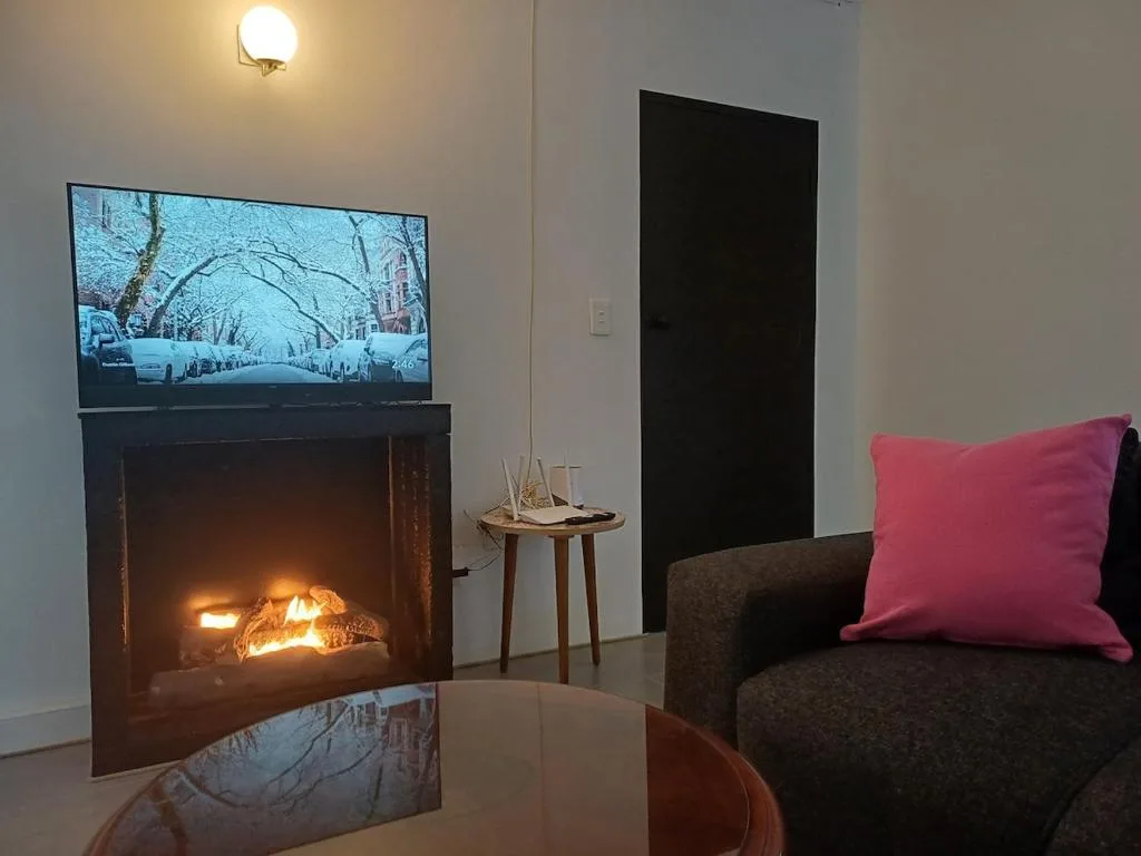 Modern lounge with fireplace, TV, dark sofa and pink cushion