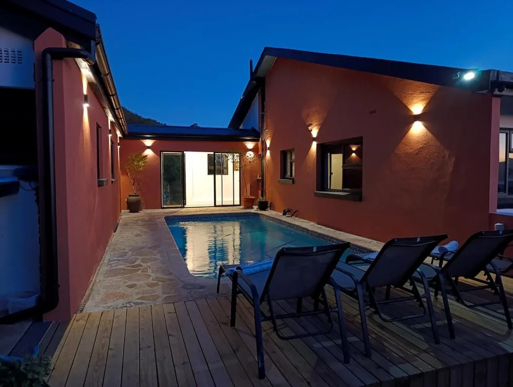Illuminated swimming pool at dusk with loungers and red-walled villa