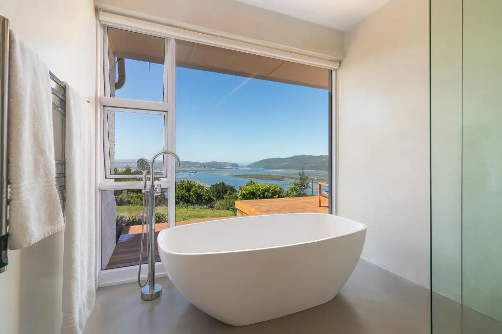 Modern freestanding bathtub with lagoon view through open doors