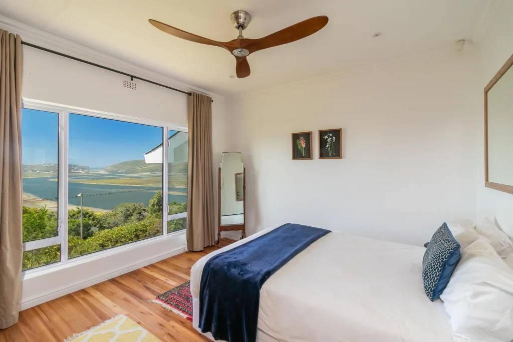 Bedroom with lagoon view through large windows and wooden ceiling fan