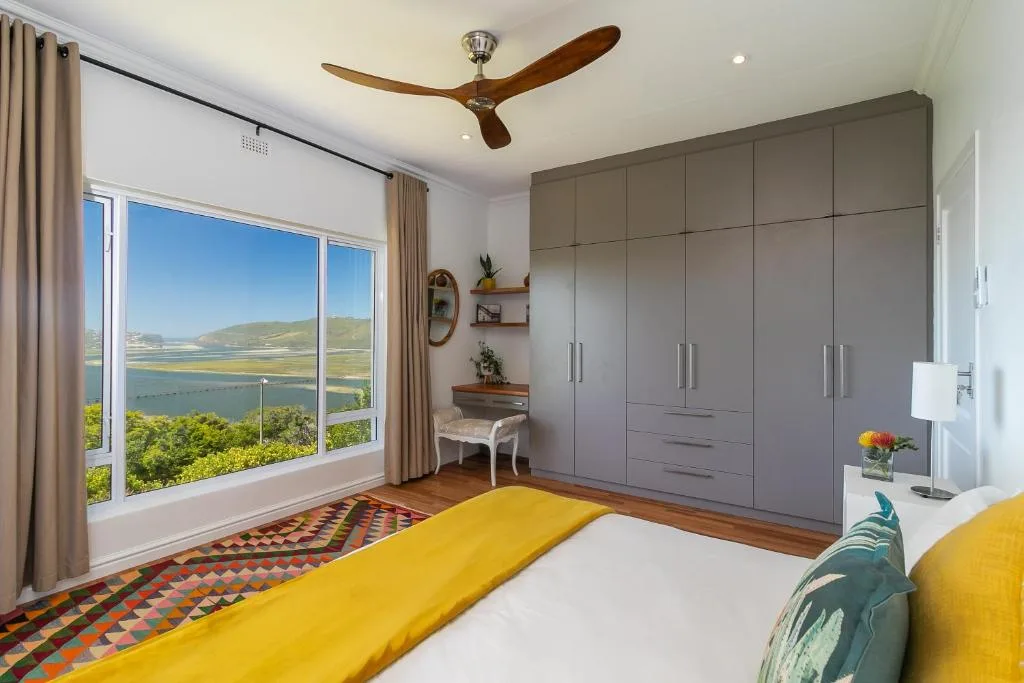 Bright bedroom with yellow bedding, large windows overlooking lagoon and mountains