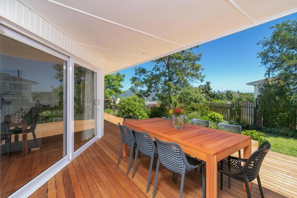 Wooden deck with dining table, chairs, and garden views under retractable awning