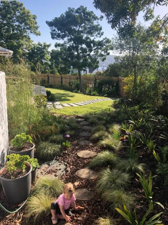 Lush garden with native plants, stepping stones, wooden fence, and lawn