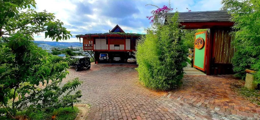 Red wooden cottage with lush green gardens and mountain valley views beyond