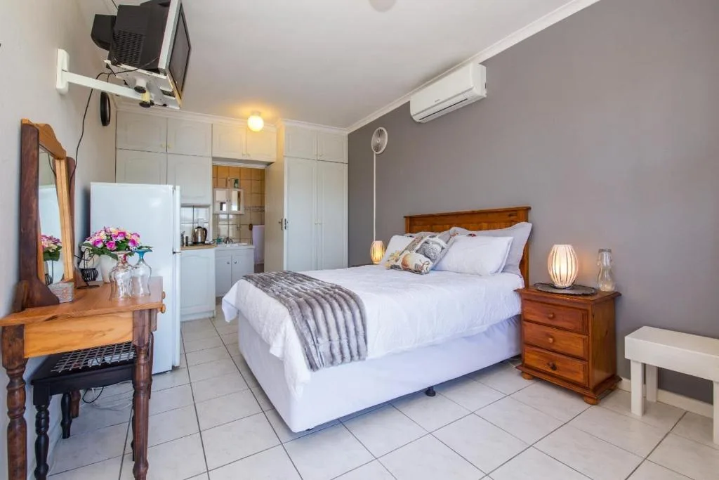 Spacious bedroom with queen bed, wooden nightstands, and kitchenette
