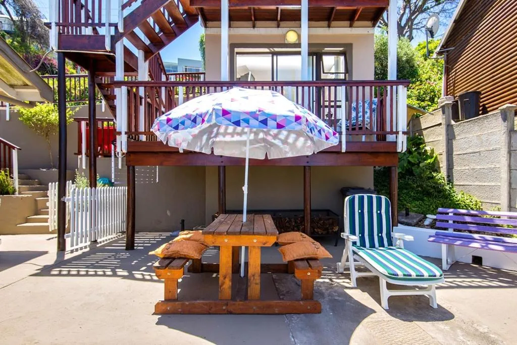 Outdoor patio with picnic table, umbrella, and loungers beneath the building