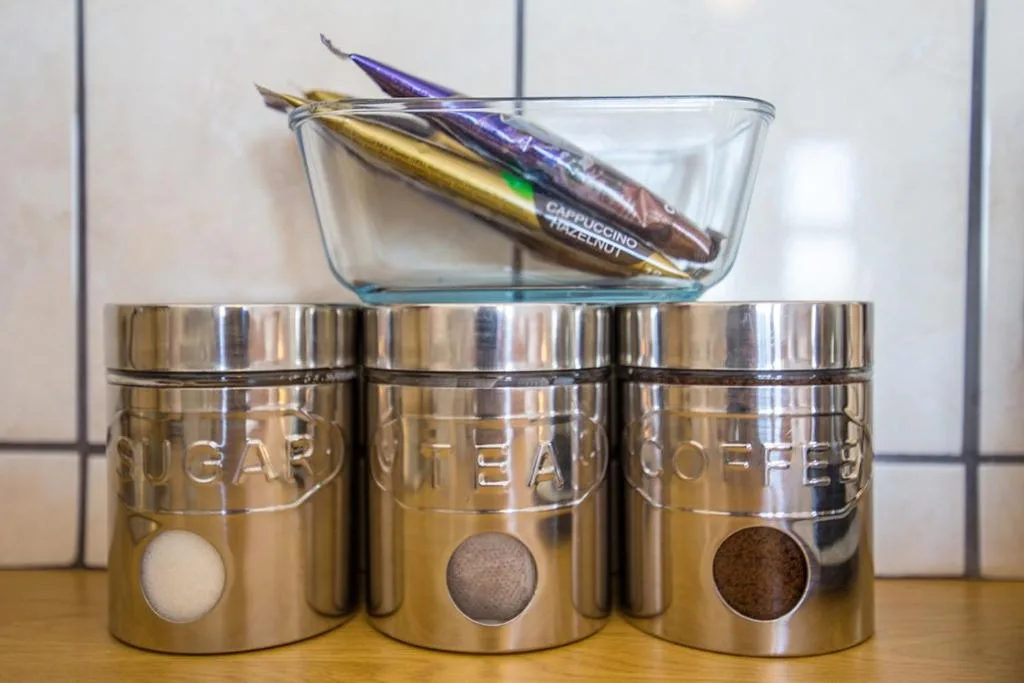 Three stainless steel kitchen canisters with glass bowl and decorative spoons