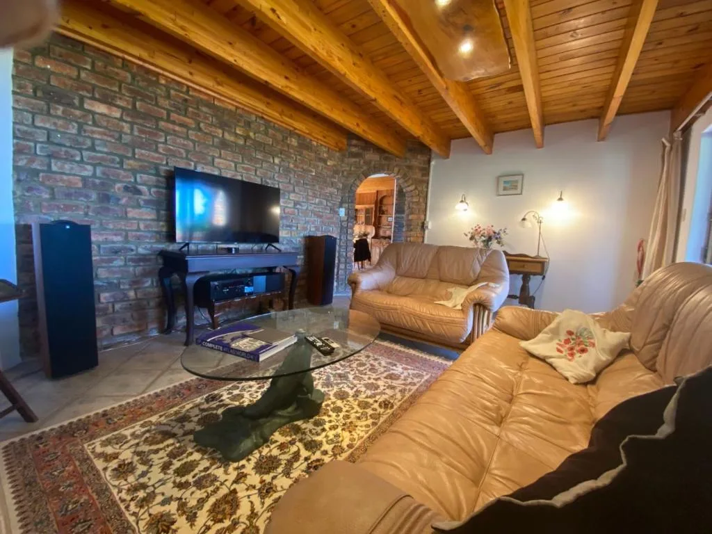 Spacious living room with cream leather sofas, exposed wooden beams, brick fireplace, and flat-screen TV