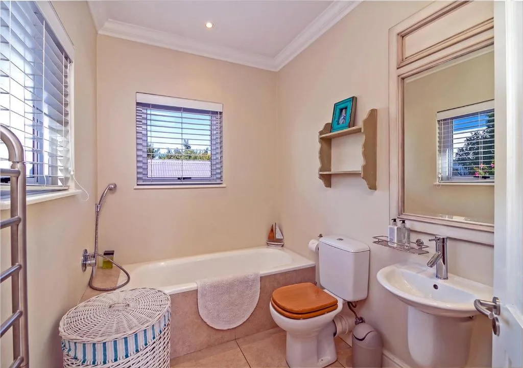 Bright bathroom with bathtub, toilet, sink, and wooden shelving