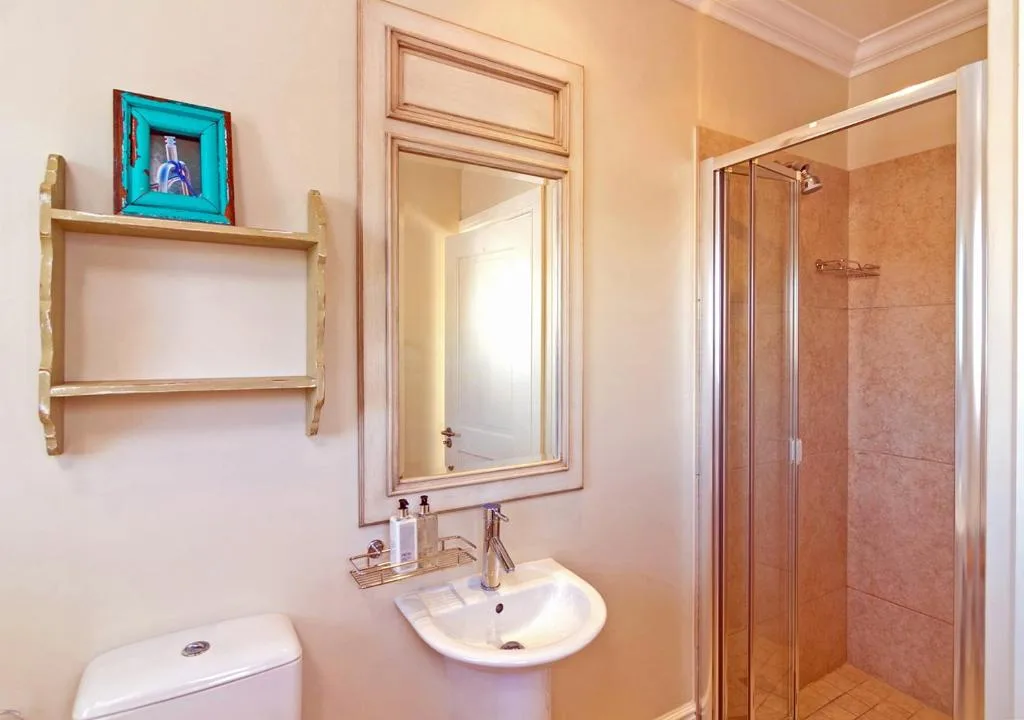 Bright bathroom with vanity sink, mirror, shelving, and enclosed shower stall