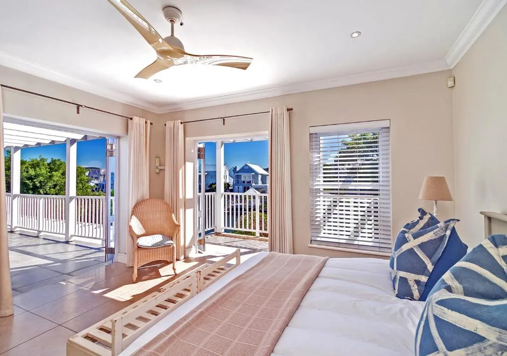 Bright bedroom with bed, rattan chair, and views to deck and canal houses