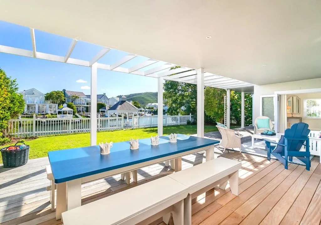 Spacious covered deck with blue dining table and waterfront views of Knysna