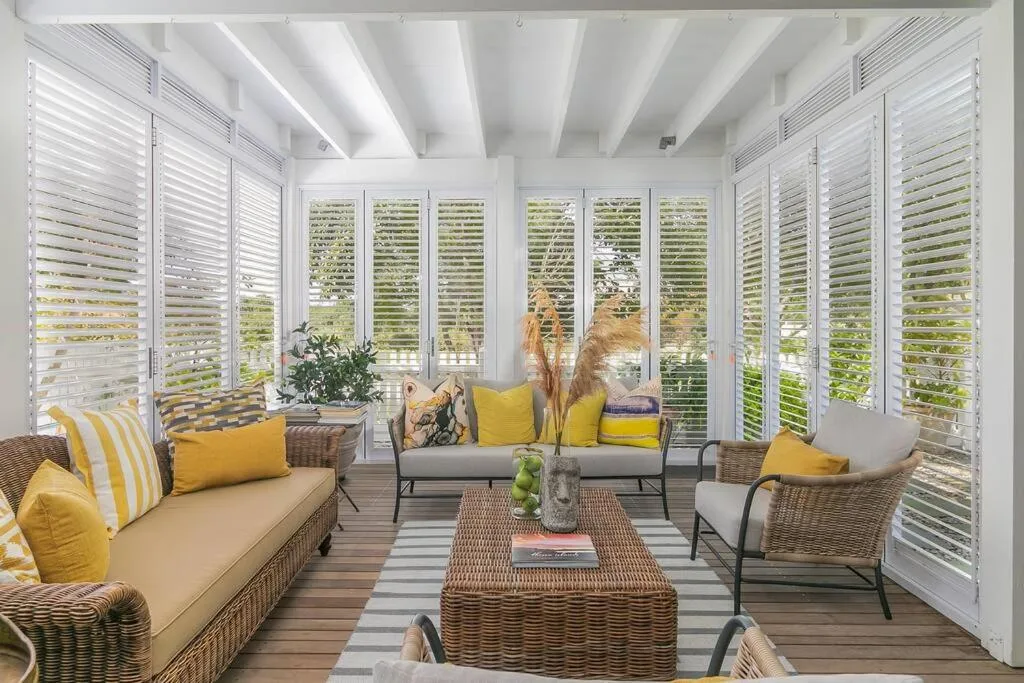 Bright sunroom with wicker furniture, yellow accents, and garden views