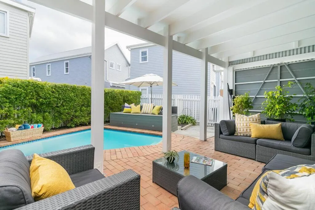 Covered patio with seating and turquoise pool beyond, white columns frame view