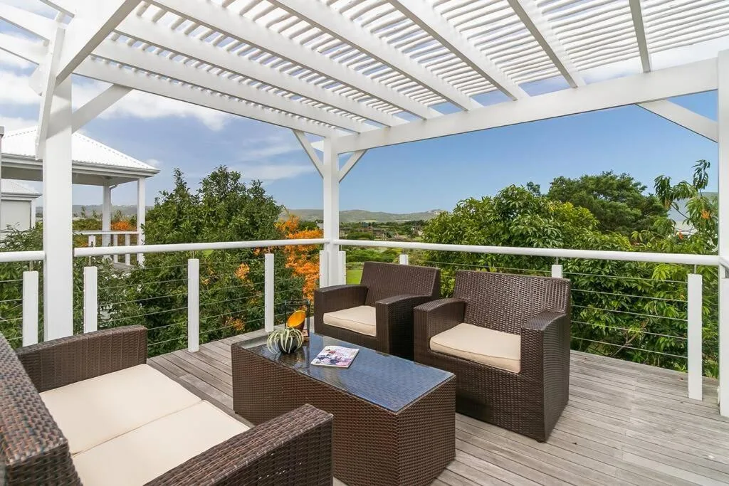 Spacious wooden deck with white pergola, wicker furniture, and mountain views
