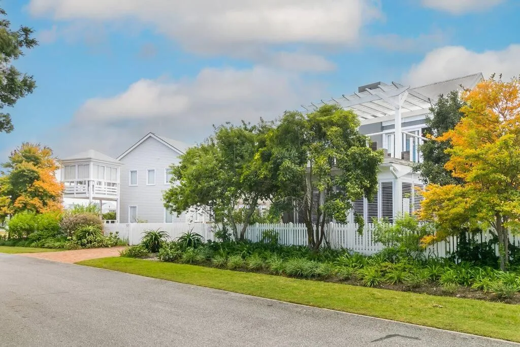 White Victorian-style house with mature trees and manicured gardens fronting driveway