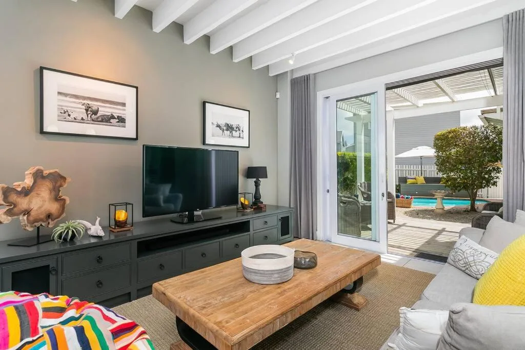 Bright living room with TV, wooden table, and outdoor deck view beyond