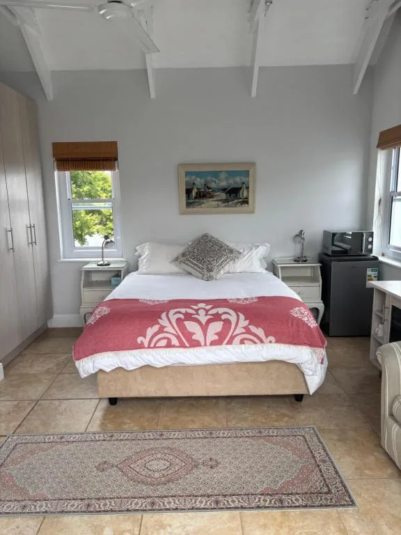 Bright bedroom with double bed, red patterned throw, windows, and wooden beams