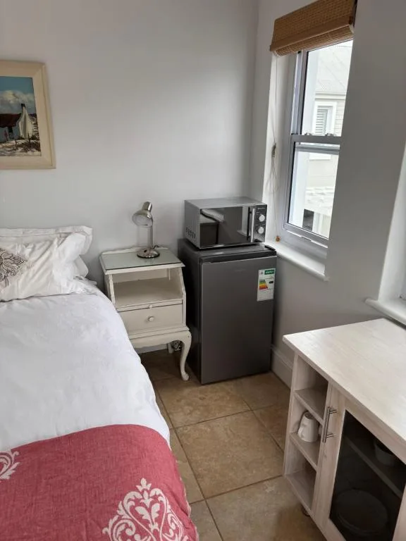 Compact bedroom with single bed, mini-fridge, microwave, and window