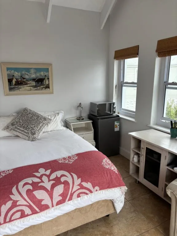 Bright bedroom with queen bed, red patterned throw, desk and small kitchenette