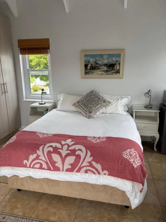 Bright bedroom with queen bed, red patterned throw, white pillows and window view