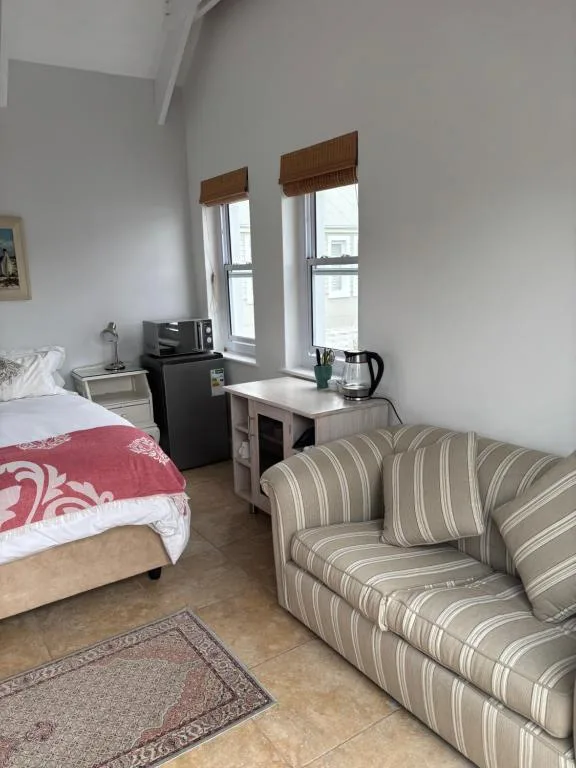 Studio bedroom with striped sofa, bed, kitchenette, and windows