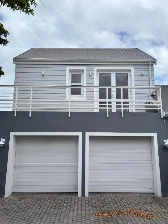Modern white cottage with garage and upper deck railing against cloudy sky