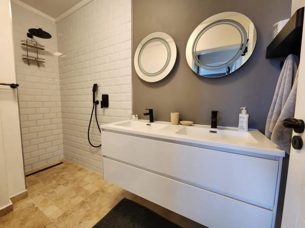 Modern bathroom with white subway tile shower, vanity, round mirrors, and black fixtures
