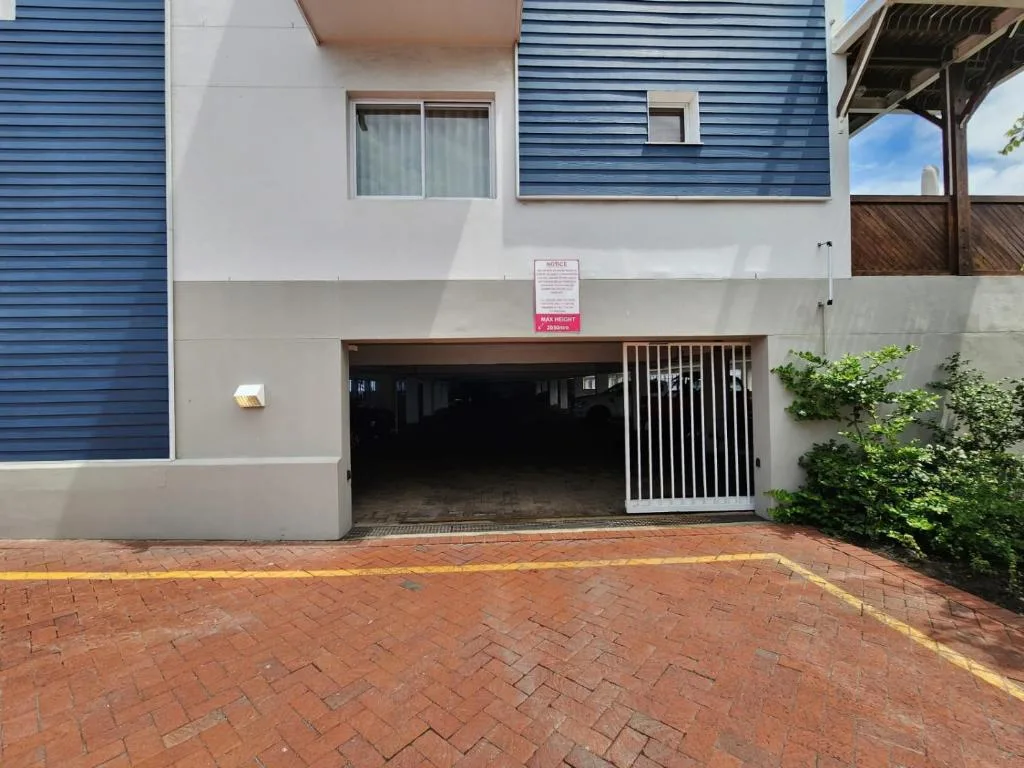 Modern apartment building facade with blue cladding, brick driveway, and garage entrance