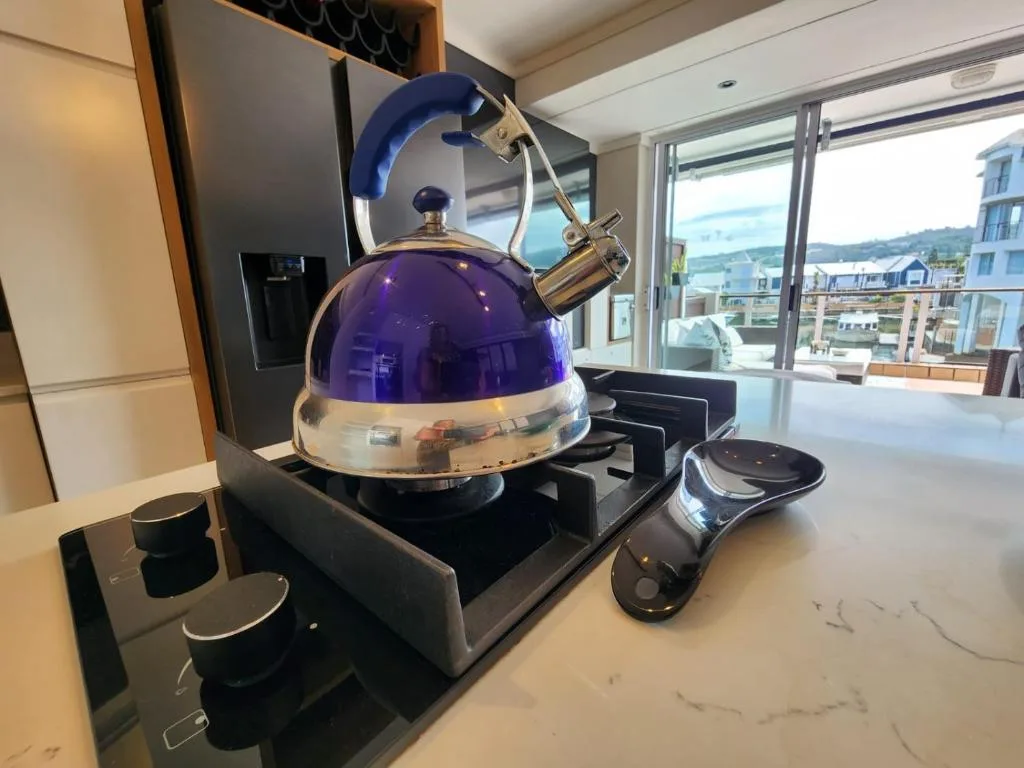 Modern kitchen stovetop with purple kettle and coastal town view beyond windows