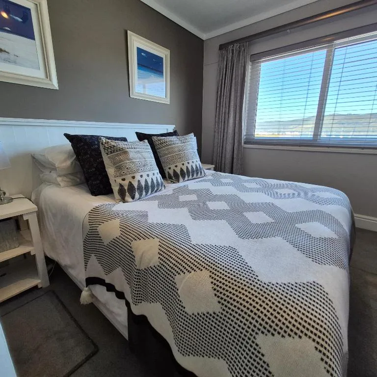 Modern bedroom with patterned bedding, decorative pillows, large windows overlooking water
