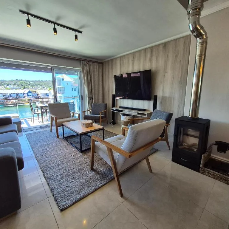 Modern lounge with cream armchairs, TV, and fireplace overlooking Knysna waterfront