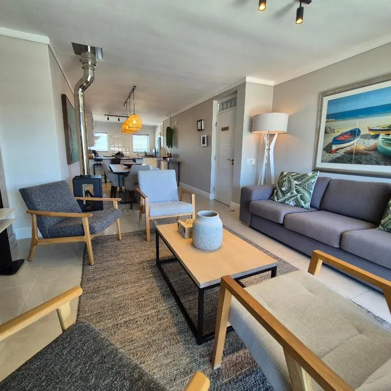 Modern living room with gray sofa, wooden armchairs, and coastal artwork