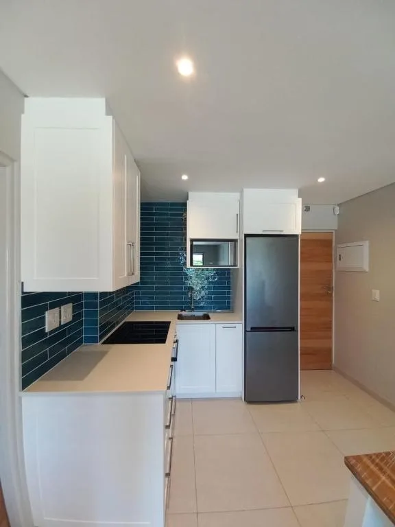 Modern kitchen with white cabinetry, dark blue tile backsplash, stainless steel appliances