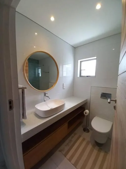Modern bathroom with circular gold mirror, white vessel sink, and toilet