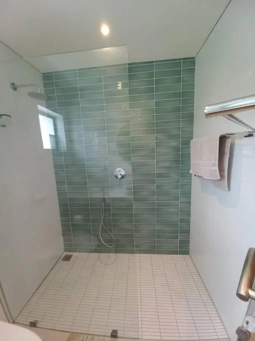 Modern walk-in shower with green tile walls and cream floor tiles