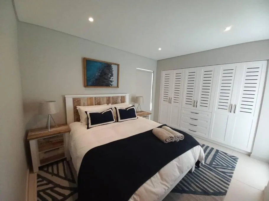 Spacious bedroom with queen bed, white shuttered wardrobe, and modern decor