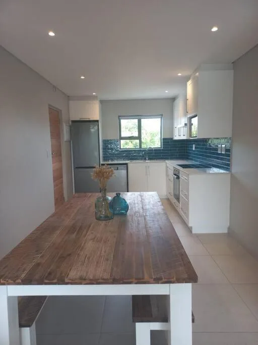 Modern kitchen with white cabinetry, blue tile backsplash, and wooden dining table