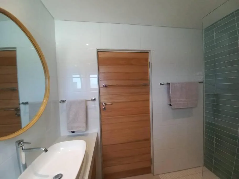 Modern bathroom with round mirror, vanity sink, wooden door, and green tile shower