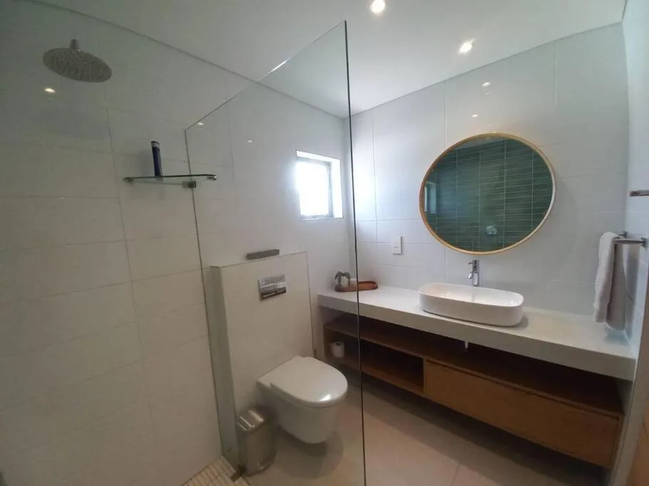 Modern bathroom with walk-in shower, toilet, and round mirror vanity