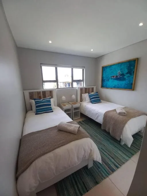 Twin bedroom with white linens, blue striped pillows, and ocean artwork