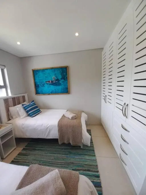 Modern bedroom with white bed, blue artwork, and built-in storage cupboards