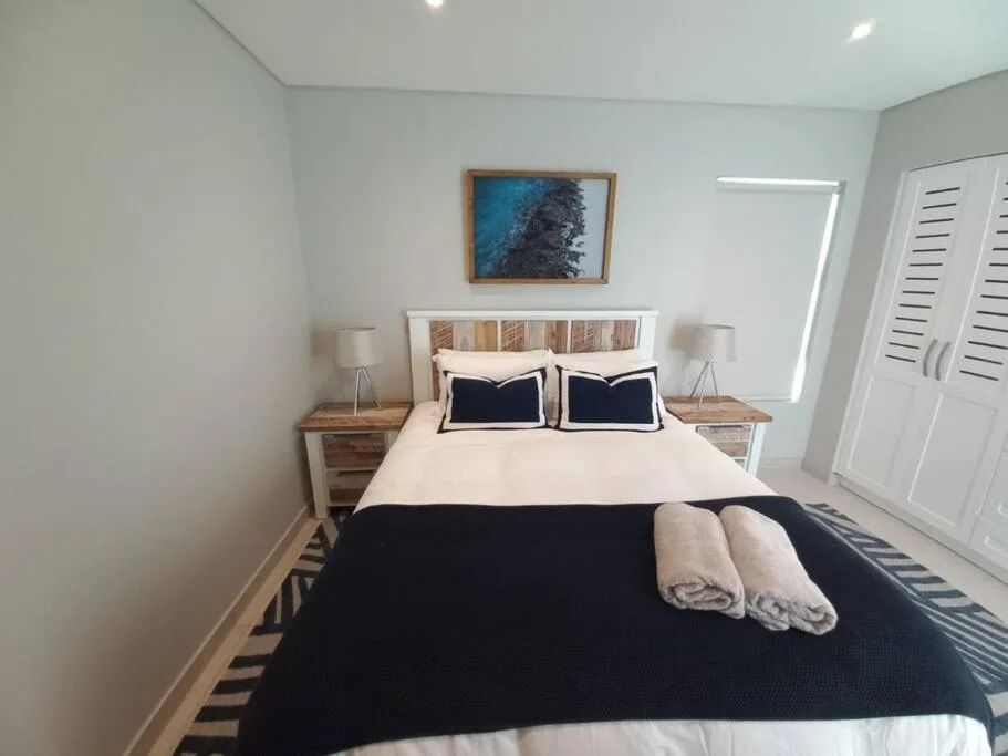 Modern bedroom with queen bed, navy bedding, wooden nightstands, and coastal artwork