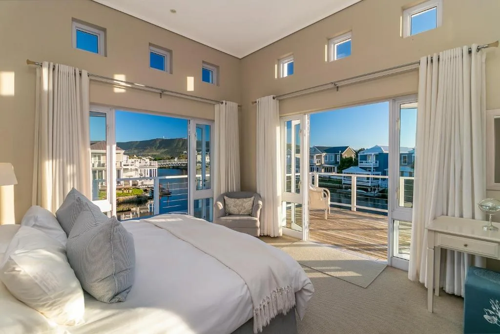 Spacious bedroom with bed overlooking Knysna waterfront and mountains through glass doors