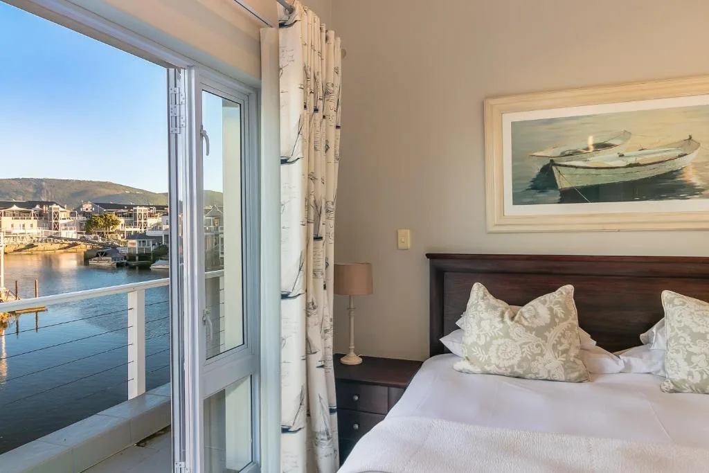 Bedroom with bed, waterfront view through glass doors, and boat artwork