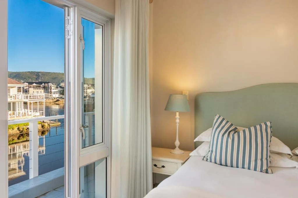 Bright bedroom with green headboard, striped pillow, and lagoon view through glass doors