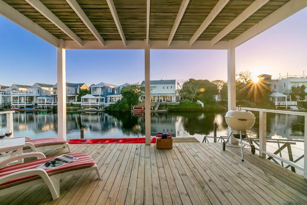 Covered waterfront deck with loungers, grill, and lagoon views at sunset